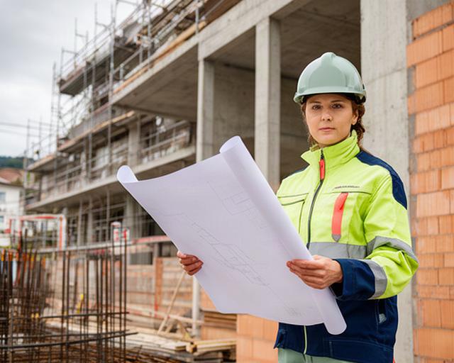 Bauleiterin mit Bauplan auf einer Baustelle in Fribourg neben einem Rohbau